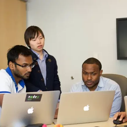 Three people working together on a laptop in an office.